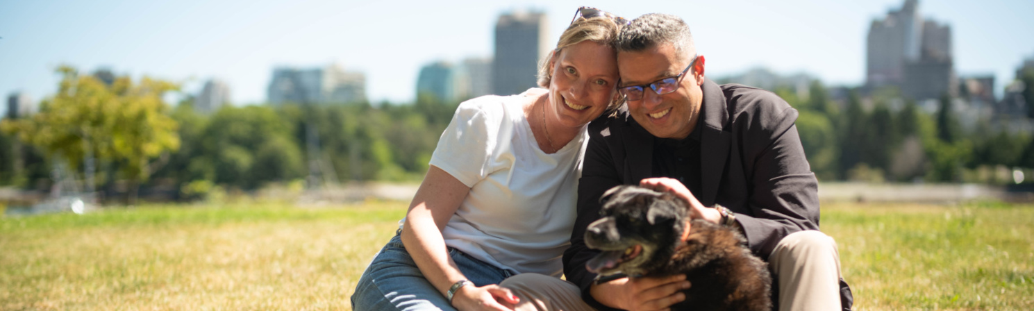 A photo of Kareem with his wife and dog in a park with the Vancouver skyline in the background